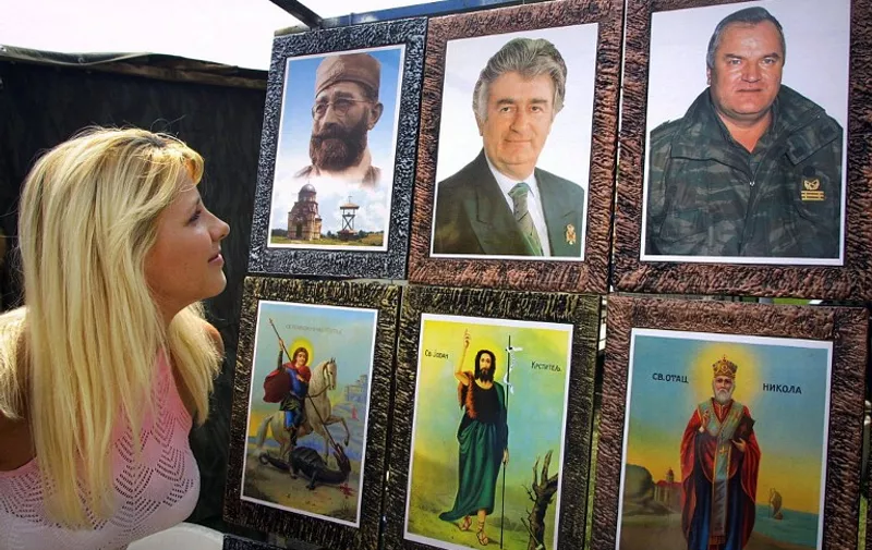 A woman watches pictures of Bosnian Serb wartime leader Radovan Karadzic (upper row, center) and his former army chief Ratko Mladic (upper row, right) - two top fugitives who have been on the run for a decade since they were charged with genocide by the UN war crimes tribunal at The Hague, and Draza Mihailovic, (upper row, left), former leader of Chetniks - Serb royalists who fought both the Nazis and the communist Partisans in World War II, together with pictures of saints important for the Serb Orthodox Church, during the market day in northwestern Bosnian town of Prijedor, 18 June 2005. Bosnian Serb authorities last year admitted to the horrific scale of the 1995 Srebrenica massacre of some 8,000 Muslims by Serb forces, but most ordinary Serbs still deny the truth about the worst single atrocity in Europe since World War II. Some 50,000 people are expected to attend ceremonies to mark the 10th anniversary of the massacre on 11 July.    AFP PHOTO STRINGER
