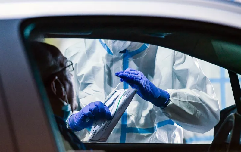A helper in a protective suit takes a sample to test the driver of a vehicle at a coronavirus testing station set up at the former Guetersloh military airport on June 30, 2020. - German Armed Forces and aid organizations have set up a smear station, where people can be tested for Covid-19 after the coronary outbreak at the Toennies meat plant. (Photo by Ina FASSBENDER / AFP)