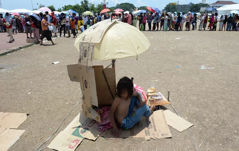 A young evacuee, one of the thousands affected by the stand-off between Philippine government forces and Muslim rebels, shelters from the scorching heat as others queue up for food distribution at an evacuation centre inside a sports complex in Zamboanga, on the southern Philippine island of Mindanao on September 20, 2013. Philippine security forces killed eight Muslim rebels on September 20 as they hunted the remnants of a guerrilla force hiding in homes of the major city and believed to be holding hostages.      AFP PHOTO / TED ALJIBE (Photo by TED ALJIBE / AFP)