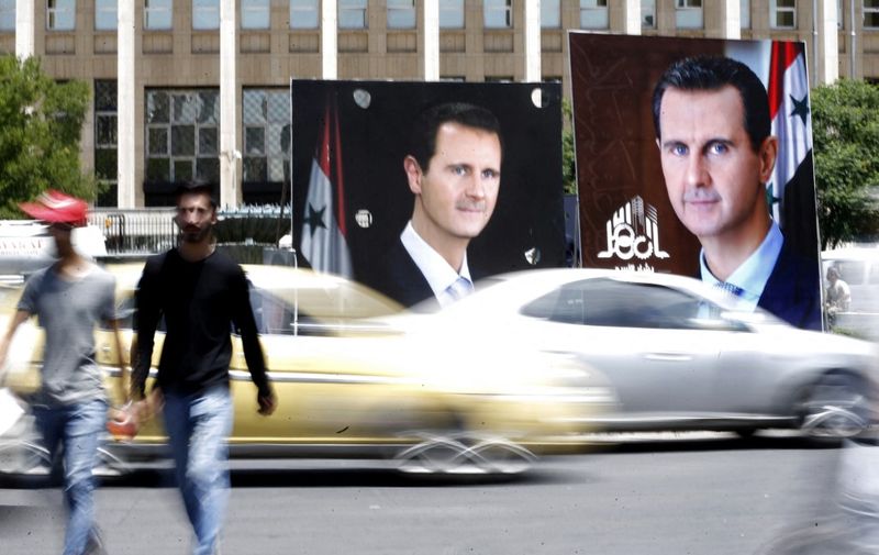 People walk next to election campaign billboards depicting Syrian President Bashar al-Assad, a candidate for the upcoming presidential vote, in the capital Damascus, on May 24, 2021. - The Syrian President Bashar al-Assad, whose family has ruled the country for over half a century, faces an election on May 26 meant to cement his image as the only hope for recovery in the war-battered country, analysts say. In the ballot, two challengers will run against him, approved by an Assad-appointed constitutional court, out of a total of 51 applicants. (Photo by LOUAI BESHARA / AFP)