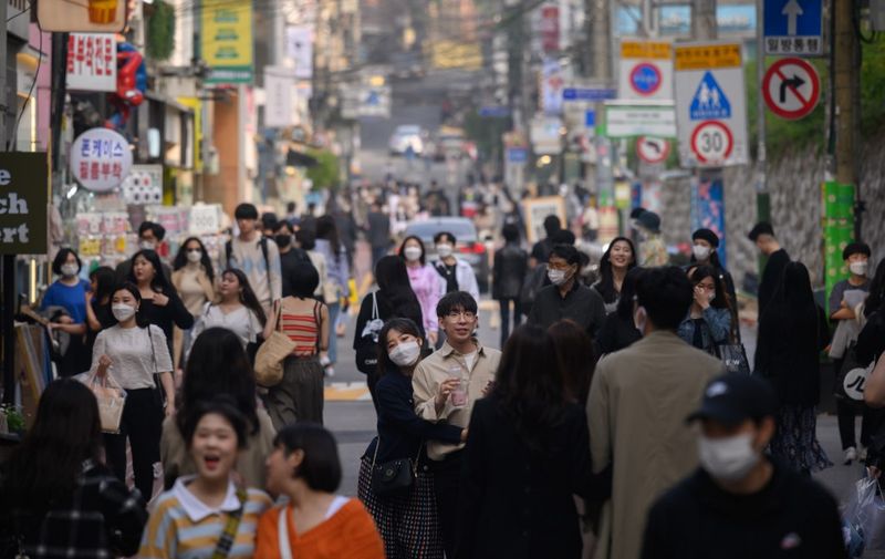 In a photo taken on May 10, 2020, people wearing face masks walk along a street in the Hongdae district of Seoul. - South Korea announced its highest number of new coronavirus cases for more than a month on May 11, driven by an infection cluster in a Seoul nightlife district just as the country loosens restrictions. (Photo by Ed JONES / AFP)