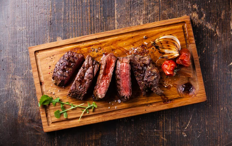 Sliced steak Ribeye with grilled onions and cherry tomatoes on cutting board on wooden background