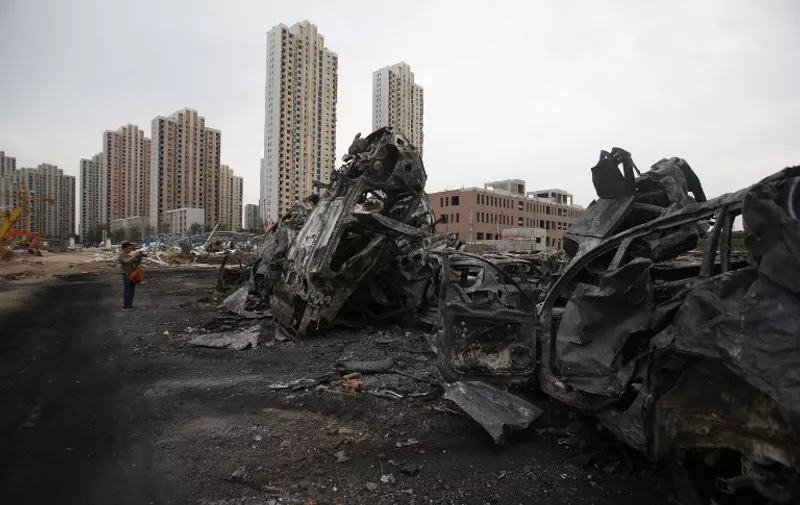 A man takes a photo of damaged cars at the site of the explosions in Tianjin on August 14, 2015.  Enormous explosions in a major Chinese port city killed at least 44 people and injured more than 500, state media reported on August 13, leaving a devastated industrial landscape of incinerated cars, toppled shipping containers and burnt-out buildings. CHINA OUT AFP PHOTO