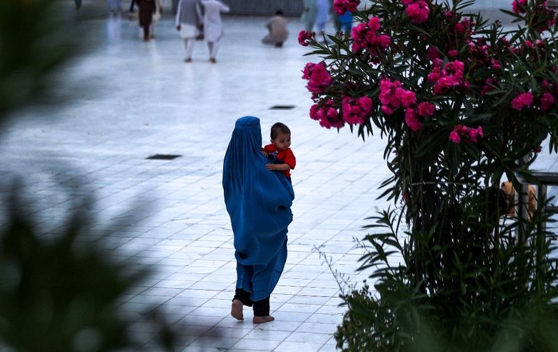 In this photograph taken on June 6, 2019, an Afghan burqa-clad woman holds a child as she walks in the courtyard of the Hazrat-e Ali shrine, also called 'Blue Mosque', during the third day of Eid al-Fitr holiday in Mazar-i-Sharif. - Muslims around the world celebrate the Eid al-Fitr holiday, which marks the end of the fasting month of Ramadan. (Photo by FARSHAD USYAN / AFP)