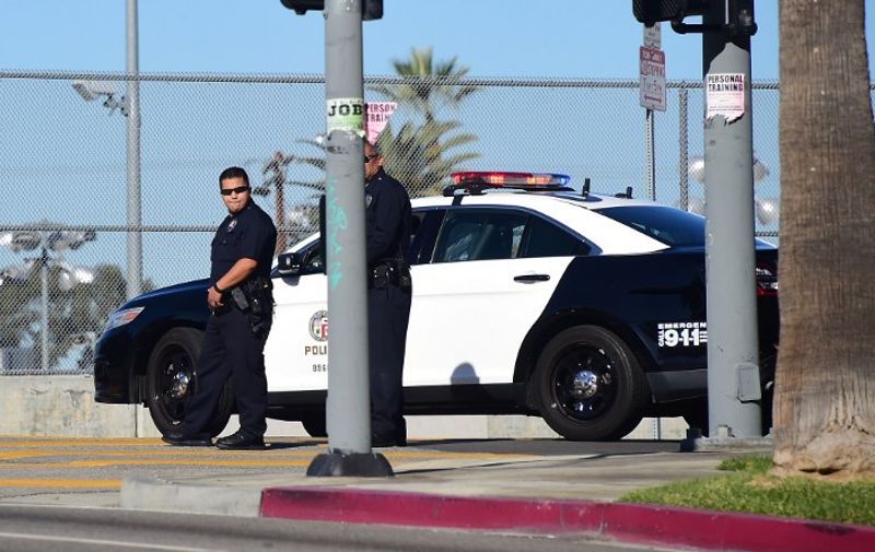 Two police officers stand at their vehicle outside a closed school near downtown Los Angeles on December 15, 2015. Los Angeles city officials on Tuesday defended their decision to shut down all public schools following a "credible" emailed threat, as authorities in New York dismissed a similar message as a hoax. Ramon Cortines, the superintendent of Los Angeles schools, said the extraordinary measure was ordered as a precaution, triggered in part by the December 2 attacks in nearby San Bernardino that left 14 people dead. AFP PHOTO/ FREDERIC J. BROWN / AFP / FREDERIC J. BROWN