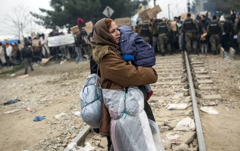 TOPSHOTS
A migrant woman holding a baby crosses a railway track in front of Macedonian policemen and migrants demonstrating, after she crossed Greek-Macedonian border near Gevgelija on November 21, 2015. Serbia and Macedonia, which lie on the main migrant route to northern Europe, have begun restricting the entry of refugees to just those from certain countries, the UN refugee agency said on November 19. AFP PHOTO / ROBERT ATANASOVSKI / AFP / ROBERT ATANASOVSKI