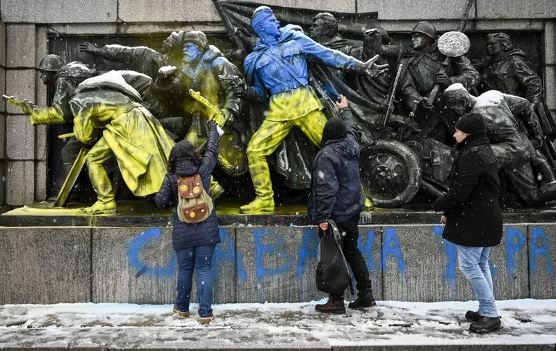 (FILES) People paint the figures of Soviet soldiers using Ukranian flag colours at the base of the Soviet Army monument in Sofia, on February 27, 2022 in reaction to Russia's invasion of Ukraine. A towering Soviet-era monument prominently featuring a soldier started to be dismantled in Sofia on Tuesday, following years of controversy between Bulgaria's opposing camps of pro-Europeans and Russophiles. (Photo by Nikolay DOYCHINOV / AFP)