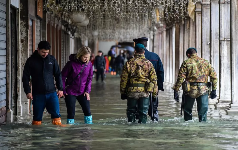 People (L), a policeman (Rear) and military men walk across a flooded arcade on November 24, 2019 in Venice during a high tide "Acqua Alta" meteorological phenomenon with a high of 140 cm expected. - Flood-hit Venice was bracing for another, though smaller, high tide on November 24, after Italy declared on November 15 a state of emergency for the UNESCO city where perilous deluges have caused millions of euros worth of damage. (Photo by Miguel MEDINA / AFP)