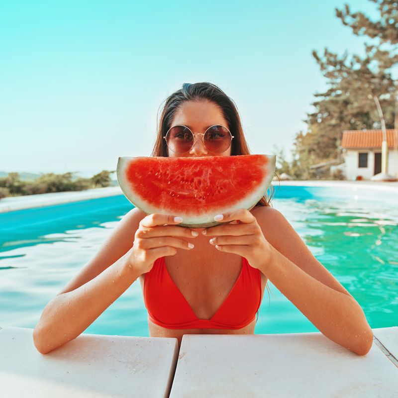 Beautiful, attractive woman enjoying in the pool, holding a watermelon