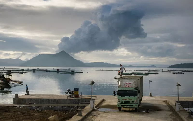 A man clears ash from the roof of his truck, before a plume of steam rising from the Taal volcano, at a fishing harbour in Laurel on January 17, 2020. (Photo by Ed JONES / AFP)
