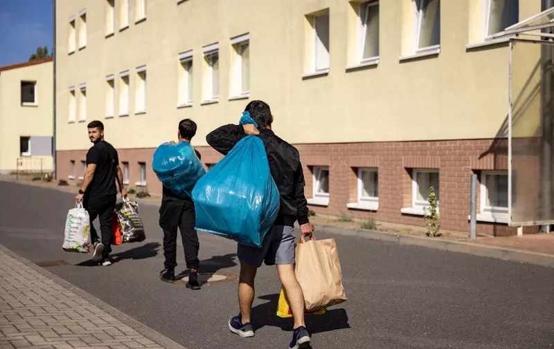 New arrivals with bags walk past a housing block at Brandenburg's Central Immigration Authority (ZABH) center, housing some 1400 asylum seekers in Eisenhuttenstadt, eastern Germany, on September 28, 2023. A short distance from the border with Poland, a former East German army barracks turned migrant processing centre is struggling to cope with a new wave of arrivals. Migrants are turning up in Germany in numbers not seen since the crisis in 2015. (Photo by Odd ANDERSEN / AFP)