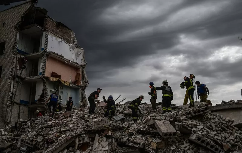 Firefighters and members of a rescue team clear the scene after a building was partialy destroyed following shelling, in Chasiv Yar, eastern Ukraine, on July 10, 2022. - At least six people were killed and five others were injured in a Russian strike on an apartment building in Chasiv Yar town, a local official said. (Photo by MIGUEL MEDINA / AFP)