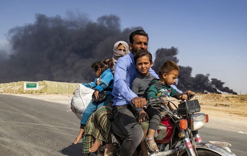 Displaced people, fleeing from the countryside of the Syrian Kurdish town of Ras al-Ain along the border with Turkey, ride a motorcycle together along a road on the outskirts of the nearby town of Tal Tamr on October 16, 2019 as they flee a deadly cross-border Turkish offensive that has sparked an international outcry, with smoke plumes of tire fires billowing in the background to decrease visibility for Turkish warplanes in the area. (Photo by Delil SOULEIMAN / AFP)