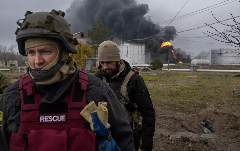 A Ukrainian rescue service member and a soldier inspect the area as black smoke rises from an oil reserve in Kherson on November 20, 2022, amid the Russian invasion of Ukraine. (Photo by BULENT KILIC / AFP)