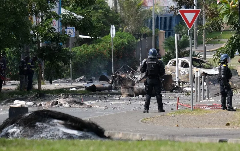 French gendarme officers guard the entrance of the Vallee-du-Tir district, in Noumea on May 14, 2024, amid protests linked to a debate on a constitutional bill aimed at enlarging the electorate for upcoming elections of the overseas French territory of New Caledonia. After scenes of violence of "great intensity" including burned vehicles, looted stores and clashes between demonstrators and the police, a curfew was decreed in Noumea, 17,000 kilometers from Paris, as the independentists of the overseas French territory of New Caledonia oppose a constitutional revision they fear will "further minimize the indigenous Kanak people". (Photo by Theo Rouby / AFP)