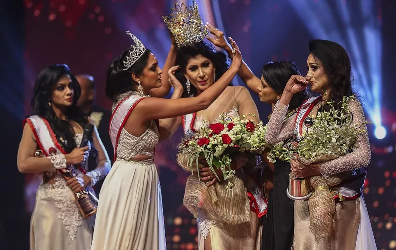 In this photograph taken on April 4, 2021, winner of Mrs. Sri Lanka 2020 Caroline Jurie (2-L) removes the crown of 2021 winner Pushpika de Silva (C) as she is disqualified by the jurie over the accusation of being divorced, at a beauty pageant for married women in Colombo. (Photo by - / AFP)