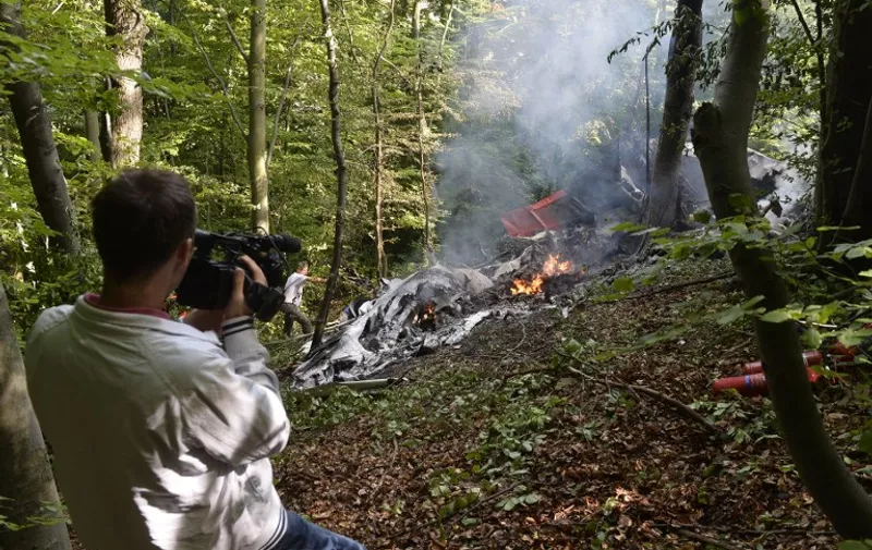 A  cameraman films next to debris of one of two collided planes near the village of Cerveny Kamen, Slovakia, on August 20, 2015. At least seven people died when two planes carrying dozens of parachutists collided in western Slovakia, the interior ministry said. AFP/Stringer