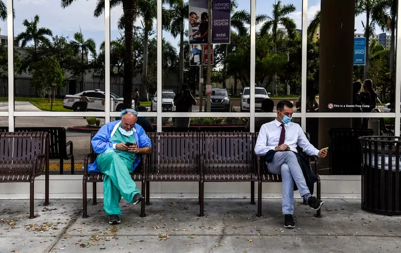 A doctor (L) wearing personal protective equipment (PPE) uses his mobile phone as he sits outside Jackson Memorial Hospital in Miami, on July 13, 2020. - Virus epicenter Florida saw 12,624 new cases on July 12 -- the second highest daily count recorded by any state, after its own record of 15,300 new COVID-19 cases a day earlier. (Photo by CHANDAN KHANNA / AFP)