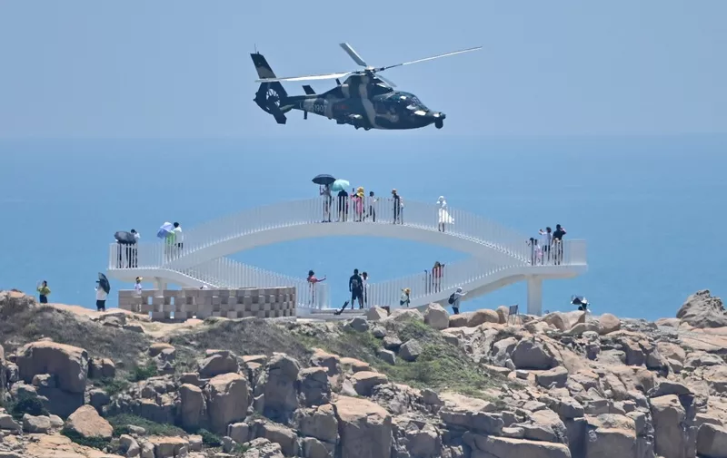 Tourists look on as a Chinese military helicopter flies past Pingtan island, one of mainland China's closest point from Taiwan, in Fujian province on August 4, 2022, ahead of massive military drills off Taiwan following US House Speaker Nancy Pelosi's visit to the self-ruled island. - China is due on August 4 to kick off its largest-ever military exercises encircling Taiwan, in a show of force straddling vital international shipping lanes following a visit to the self-ruled island by US House Speaker Nancy Pelosi. (Photo by Hector RETAMAL / AFP)