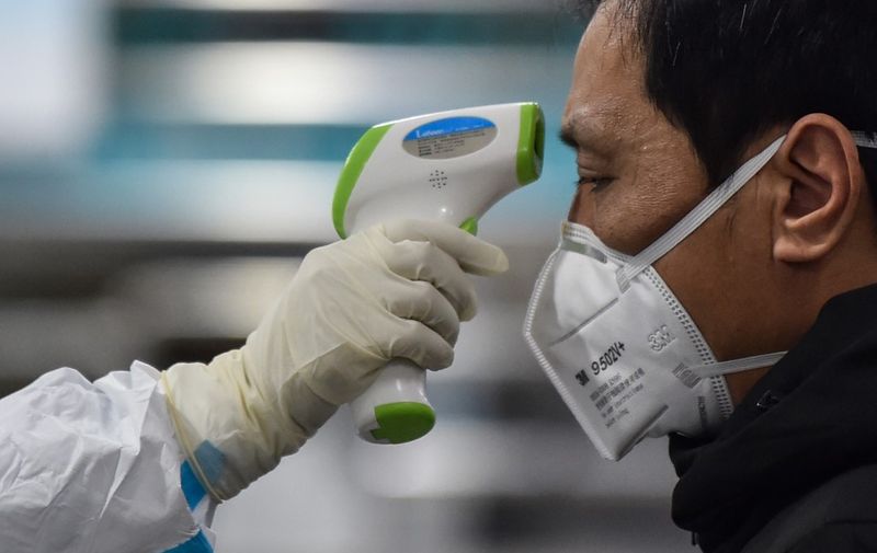 A medical staff member (L) wearing protective clothing to help stop the spread of a deadly virus which began in the city, takes the temperature of a man (R) at the Wuhan Red Cross Hospital in Wuhan on January 25, 2020. - The Chinese army deployed medical specialists on January 25 to the epicentre of a spiralling viral outbreak that has killed 41 people and spread around the world, as millions spent their normally festive Lunar New Year holiday under lockdown. (Photo by Hector RETAMAL / AFP)