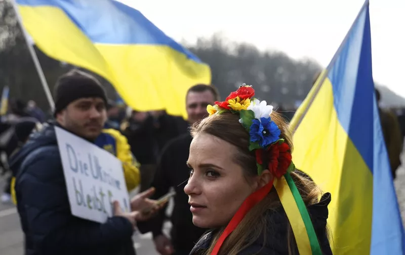 A protestors with flowers in her hair and a Ukrainian flag marches on the Strasse des 17. Juni road between the Victory column and the Brandenburg Gate in Berlin to demonstrate for peace in Ukraine on February 27, 2022. - More than 100,000 people turned up at the march in solidarity with Ukraine, police said, with many protesters dressed in the blue and yellow colours of the Ukraine flag. (Photo by Odd ANDERSEN / AFP)