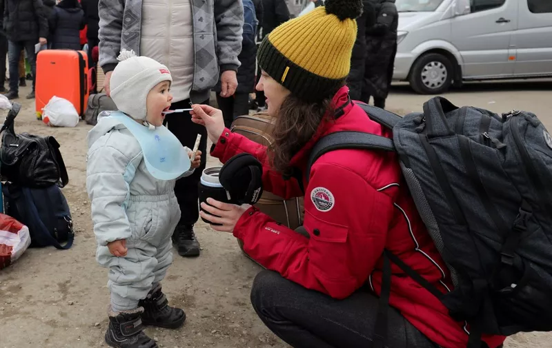 A woman feeds a toddler as people fleeing the conflict in Ukraine wait to board buses after crossing the Moldova-Ukraine border checkpoint near the Moldovan town of Palanca, on March 14, 2022, after Russia' military invasion of Ukraine. - The number of refugees who have fled Ukraine since the Russian invasion began on February 24 has topped 2.8 million, the United Nations said today. (Photo by GIL COHEN-MAGEN / AFP)