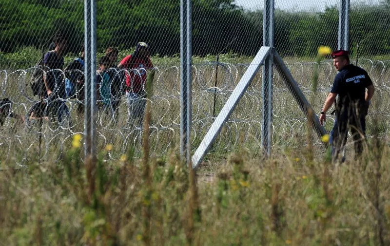 Migrant people stand on Serbian side of the metal fence beside a Hungarian police official near the Hungarian village of Asotthalom of the Hungarian-Serbian border on August 27, 2015. As Hungary scrambles to ramp up defences on its border with Serbia, refugees continued to surge into the country in record numbers, police figures confirmed.  AFP PHOTO / ATTILA KISBENEDEK