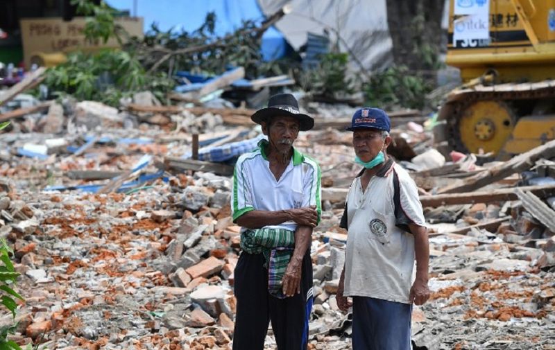Two residents look on as damaged houses are being destroyed by workers using an excavator after an earthquake hit the area of Gangga on August 12, 2018.
An earthquake on the Indonesian island of Lombok has killed 387 people, authorities said on August 11, adding hundreds of thousands of displaced people were still short of clean water, food and medicine nearly a week on. / AFP PHOTO / ADEK BERRY