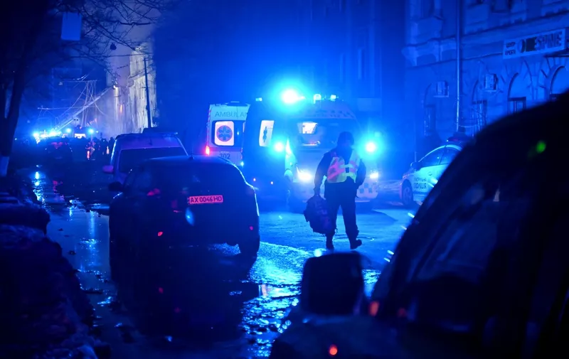 A law enforcement officer walks past ambulances parked at the site of a missile attack in Kharkiv late on January 16, 2024. At least 17 people were wounded in Russian strikes on residential buildings in the city centre on January 16, 2024, the regional governor said. (Photo by SERGEY BOBOK / AFP)