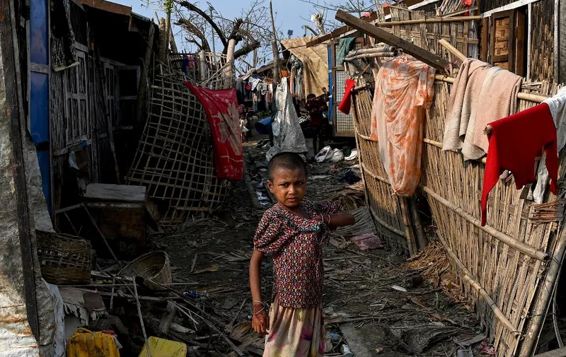 A girl stands next to her destroyed house at Ohn Taw Chay refugee camp in Sittwe on May 16, 2023, in the aftermath of Cyclone Mocha's landfall. The death toll in cyclone-hit Myanmar rose to 60 on May 16, according to local leaders and junta-backed media, as villagers tried to piece together ruined homes and waited for aid and support. (Photo by SAI Aung MAIN / AFP)