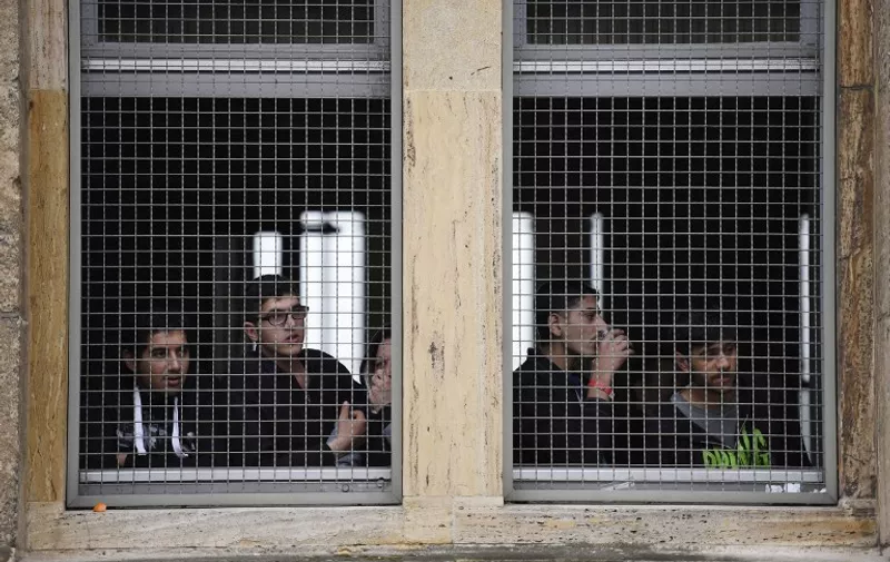 Refugees look out of a window at the former airport Tempelhof that now hosts refugees in Berlin, on November 29, 2015 after a brawl erupted among refugees. Clashes broke out between hundreds of asylum seekers armed with knives and sticks at a shelter in Berlin, in the second  mass brawl to erupt over the weekend at crowded migrant accommodations in Germany. AFP PHOTO / ODD ANDERSEN / AFP / ODD ANDERSEN