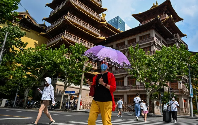A pedestrian crosses a street while holding an umbrella to protect from the sun amid record high temperatures in Shanghai on August 11, 2022. (Photo by Hector RETAMAL / AFP)