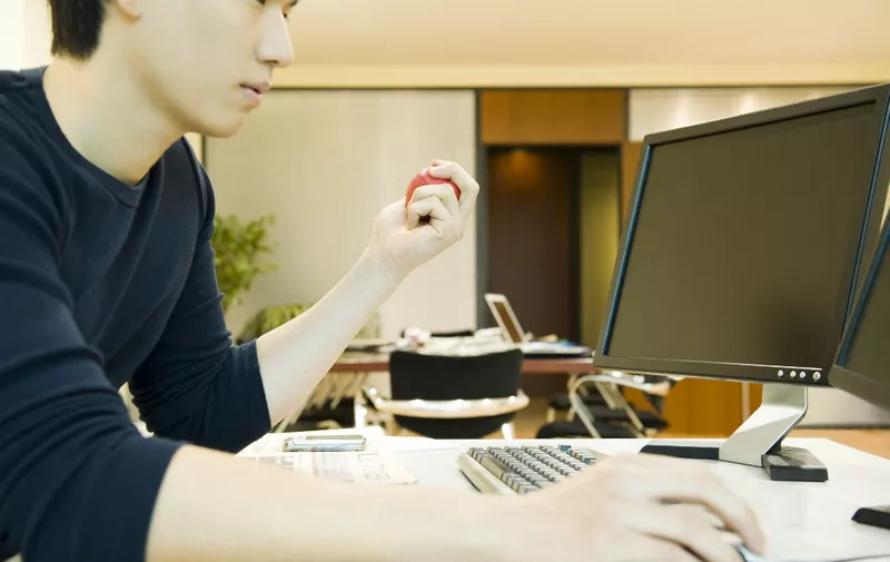 Office worker using computer, squeezing stress ball with one hand (Photo by Eric Audras / AltoPress / PhotoAlto via AFP)