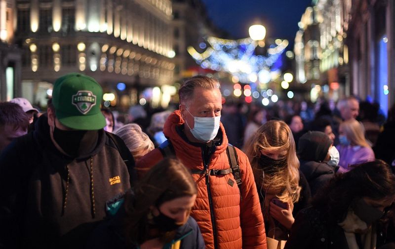 Shoppers, some wearing face coverings, cross Oxford Street in central London on December 4, 2021, as compulsory mask wearing in shops has been reintroduced in England as fears rise over the Omicron variant of Covid-19. (Photo by Daniel LEAL / AFP)