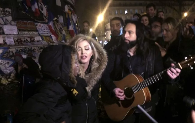 US singer Madonna (C) sings next to her guitarist Monte Pittman (C-R) and her son David Banda (L) on December 10, 2015 at the place de la Republique in Paris at a makeshift memorial in tribute to victims of November 13 terror attacks in Paris.
Singer Madonna made an emotional appeal following November 13 attacks in Paris that killed 130, shouting "We will not bend down to fear!" during a concert in the French capital. The star then moved to Place de la Republique, which has become an unofficial hub for mourners of the attacks, and sang a series of songs to a small crowd. / AFP / Jules Mahe