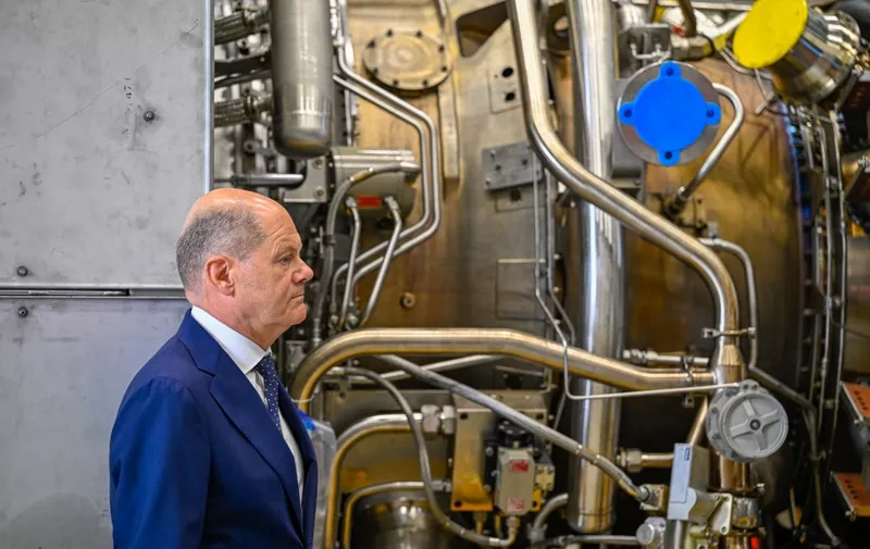 German Chancellor Olaf Scholz stands in front of a turbine of the Nord Stream 1 pipeline during a visit on August 3, 2022 at the plant of Siemens Energy in Muelheim an der Ruhr, western Germany, where the engine is stored after maintenance work in Canada. - German Chancellor Olaf Scholz on August 3, 2022 said Russia responsible for blocking the delivery of the turbine it needs to keep gas flowing to Europe. Russian energy giant Gazprom had halted operation of one of the last two operating turbines for the Nord Stream 1 pipeline due to the "technical condition of the engine" and drastically cut gas deliveries to Europe. (Photo by SASCHA SCHUERMANN / AFP)