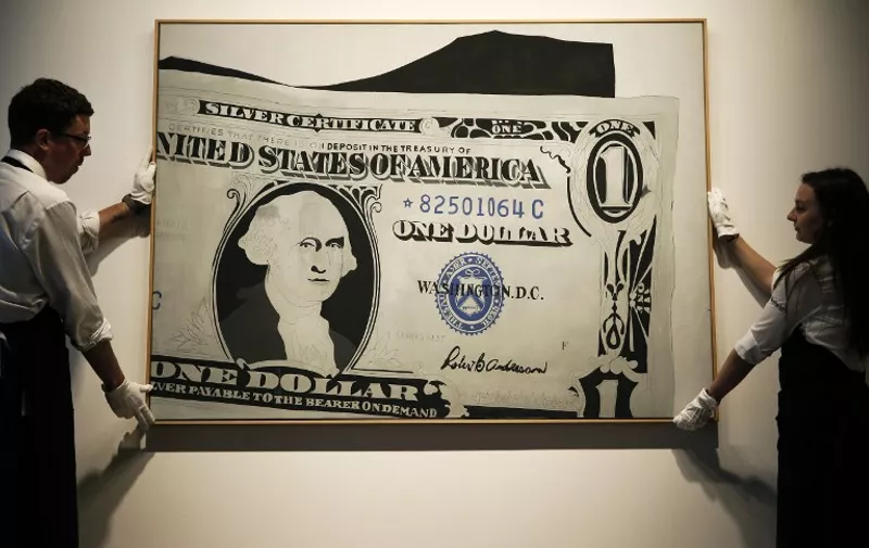 Sotheby's employees pose with a piece of artwork entitled "Silver Certificate, 1962," an acryllic on canvas by US artist Andy Warhol, valued at 13-18 million British pounds (19.8-27.5 million US dollars, 17.8-24.6 million Euros) at Sotheby's auction house in London on June 8, 2015. Sotheby's are to offer a museum-quality private collection of 21 works by several artists inspired by the US dollar motif.  AFP PHOTO/ADRIAN DENNIS

RESTRICTED TO EDITORIAL USE, MANDATORY MENTION OF THE ARTIST UPON PUBLICATION, TO ILLUSTRATE THE EVENT AS SPECIFIED IN THE CAPTION