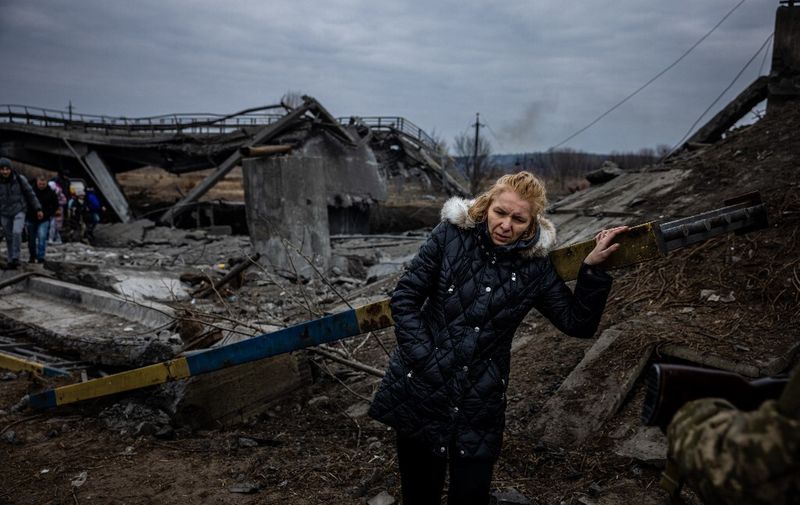 A woman takes a rest after crossing a destroyed bridge as she evacuates from the city of Irpin, northwest of Kyiv, on March 7, 2022. - Ukraine dismissed Moscow's offer to set up humanitarian corridors from several bombarded cities on Monday after it emerged some routes would lead refugees into Russia or Belarus. The Russian proposal of safe passage from Kharkiv, Kyiv, Mariupol and Sumy had come after terrified Ukrainian civilians came under fire in previous ceasefire attempts. (Photo by Dimitar DILKOFF / AFP)