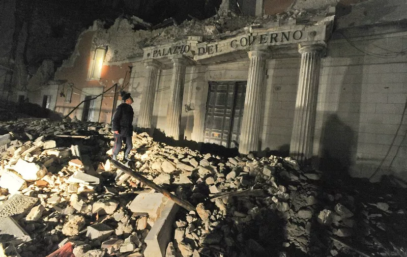 Italian Carabiniere stands on heaps of rubble during a night patrol in front of the collapsed government's local headquarters palace, in main street of the devastated city of L'Aquila on April 14, 2009, epicentre of the April 6 earthquake that stroke the Abruzzo region.  AFP PHOTO / ANDREAS SOLARO (Photo by ANDREAS SOLARO / AFP)