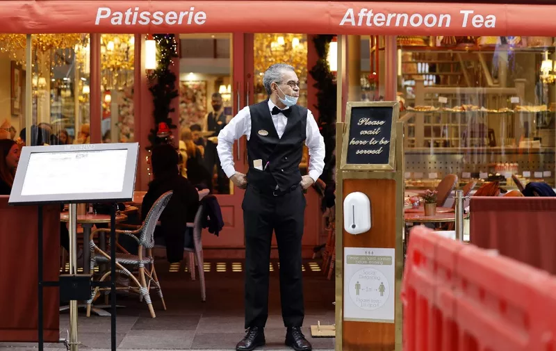 A hospitality industry worker waits for customers outside a restaurant in London on December 21, 2021. - Britain on Tuesday launched a £1.0 billion support package for Covid-hit businesses, as staff absences from rising cases of the Omicron coronavirus variant began to bite in the run-up to Christmas. Finance minister Rishi Sunak said some 200,000 firms would be eligible for one-off grants to offset losses from what is normally the busiest time of year. (Photo by Tolga Akmen / AFP)