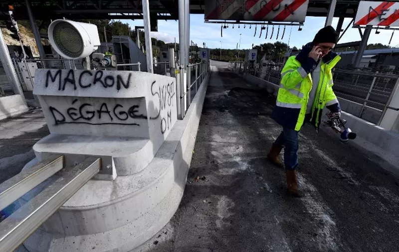 A worker of French construction group Vinci walks near a graffiti reading "Macron go away" a day after the highway toll was set on fire on December 18, 2018 in Bandol, near Marseille, southern France, following Yellow vests protests. - 17 persons have been placed in police custody after a fire burnt a highway toll in the night of December 17, 2018. (Photo by GERARD JULIEN / AFP)
