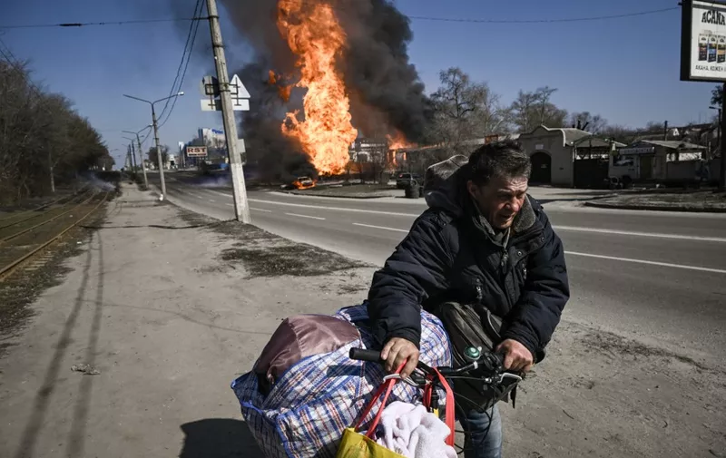 A man flees with his belongings as fire engulfs a vehicle and building following artillery fire on the 30th day on the invasion of the Ukraine by Russian forces in the northeastern city of Kharkiv on March 25, 2022. - Russian strikes targeting a medical facility in Ukraine's second city of Kharkiv on March 25, 2022, killing at least four civilians and wounding several others, Ukrainian officials said. (Photo by Aris Messinis / AFP)