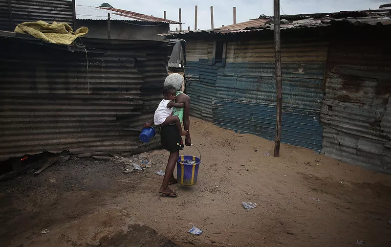 MONROVIA, LIBERIA - AUGUST 15:  Children carry warm water for bathing in a slum, where most residents have neither water nor electricity in their homes on August 15, 2014 in Monrovia, Liberia. Poor sanitation and close living quarters have contributed to the spead of the Ebola virus, which is transmitted through bodily fluids. The epidemic has killed more than 1,000 people in four West African countries.  (Photo by John Moore/Getty Images)