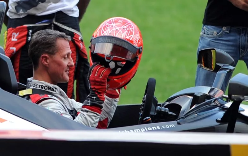 German Formula One driver Michael Schumacher (L) puts on a helmet during a practice session ahead of the annual Race of Champions (ROC) at Rajamangala Stadium in Bangkok on December 15, 2012. The Race of Champions (ROC) will take place in Thailand between December 14 and 16 and brings together heavyweights from all motor racing disciplines in the same type of car.    AFP PHOTO / PORNCHAI KITTIWONGSAKUL